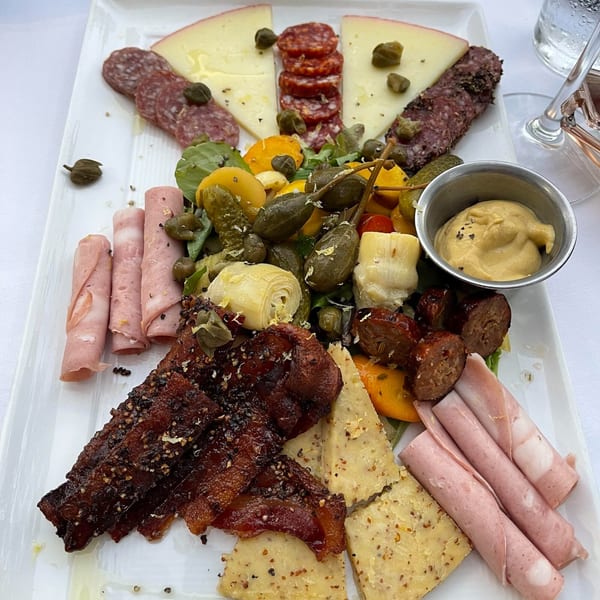 A large charcuterie board from Polo Grill with various meats, cheeses, pickled vegetables, and mustard.