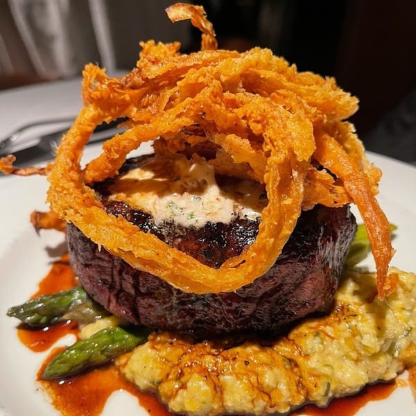 Polo Grill's steak with crispy fried onions, asparagus, and mashed potatoes on a white plate.