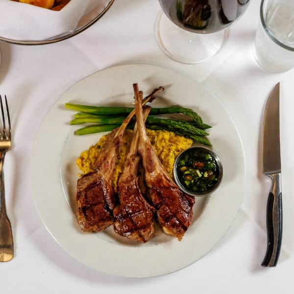 Grilled lamb chops with asparagus, yellow rice, and green sauce on a white plate.