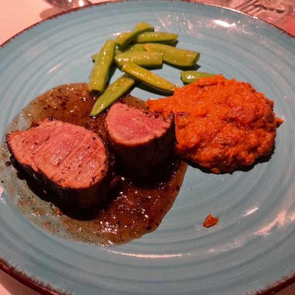 Two slices of medium-rare steak with sauce, snap peas, and orange mashed vegetables on a blue plate.