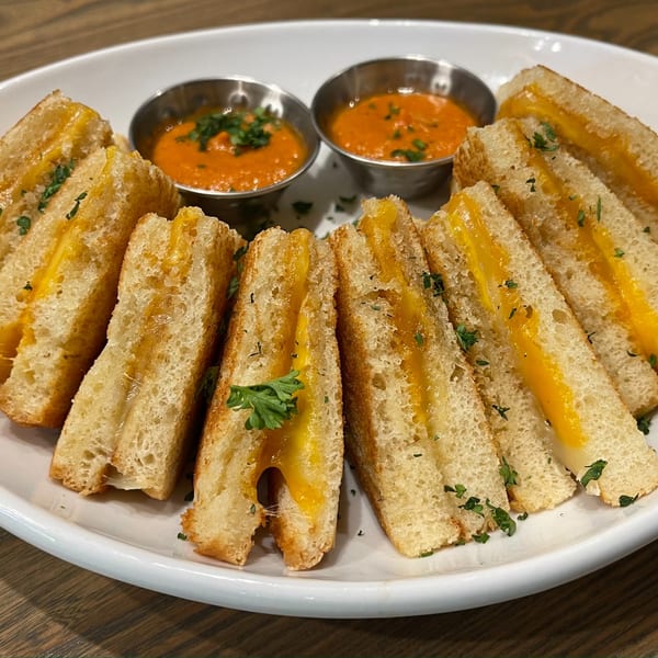 Grilled cheese triangles with melted cheddar and parsley, served with two cups of tomato soup.